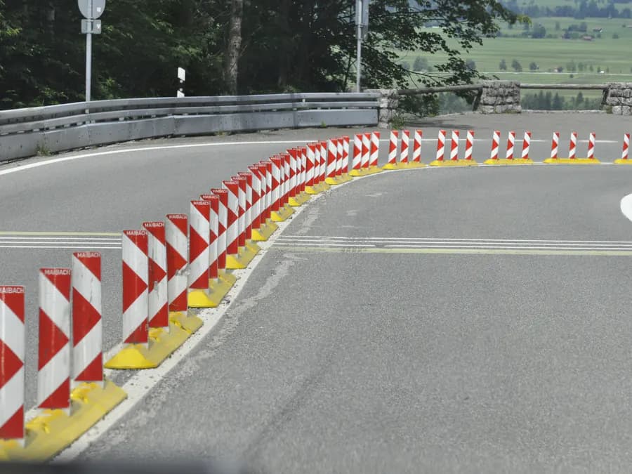 Rot-weiße Leitbaken auf gelben Fußelementen säumen eine enge Kurve einer Bergstraße