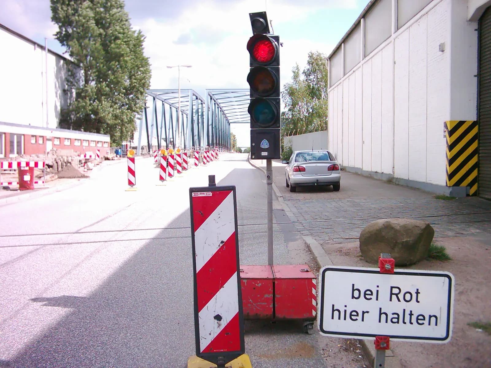 Mobile Baustellenampel auf rotem Akkukasten mit Leitbake und Zusatzzeichen „bei Rot hier halten“ vor einer Fahrbahnverengung